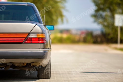 Preview: Back view of silver car parked on paved street in quiet area on sunny bright background