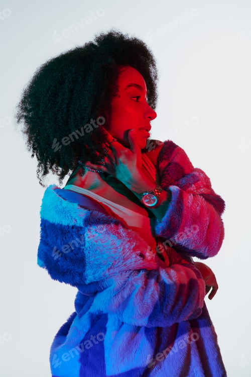 Preview: attractive african american female model in faux fur looking away in lights, fashion concept