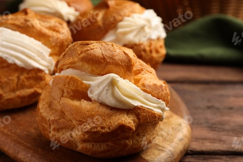 Preview: Delicious profiteroles with cream filling on wooden table, closeup
