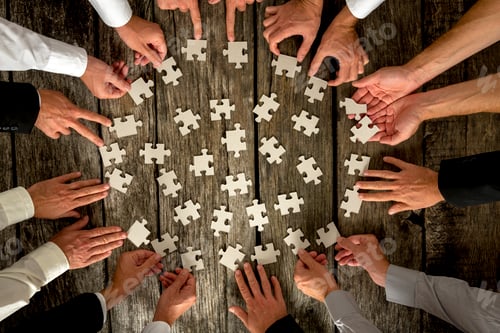 Preview: Businessmen Hands Holding Puzzle Pieces on Table