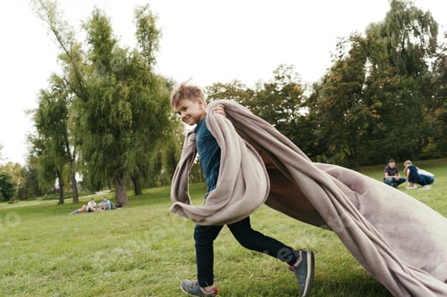 Preview: Cheerful boy running with a flying blanket in the park