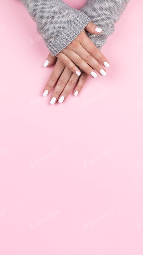 Preview: Hands in sweater with white nails on pink background