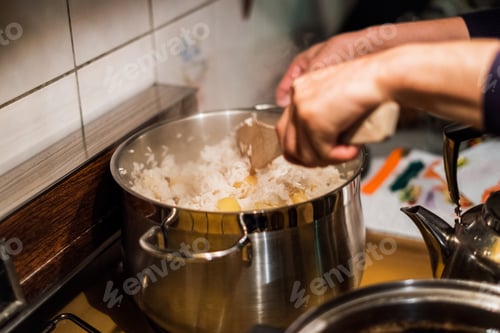 Preview: Hand chef using wooden flipper mixing rice with potato in pot