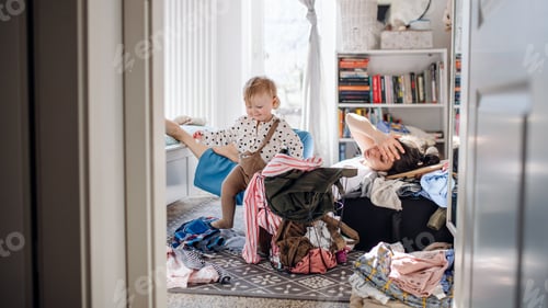 Preview: Tired mother with small toddler daughter in messy bedroom at home, resting.