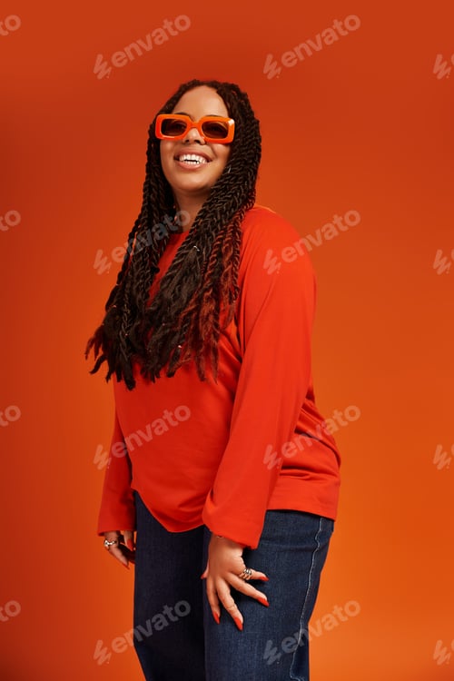 Preview: Stylish Black woman with braids enjoys a vibrant moment against an orange backdrop