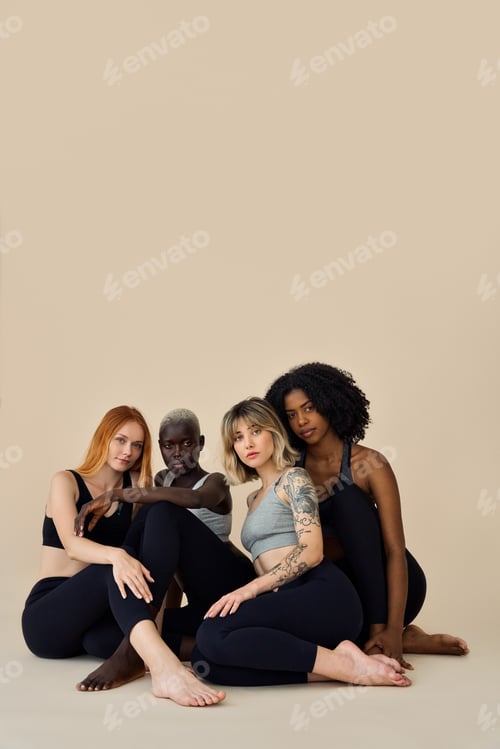 Preview: Fit healthy cool diverse girls wearing sportswear sitting at beige background.