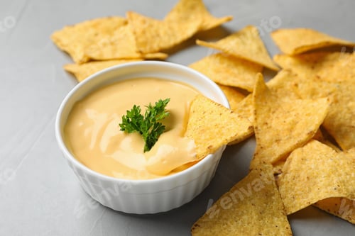 Preview: Tasty cheese sauce with Mexican nachos chips on grey table, closeup