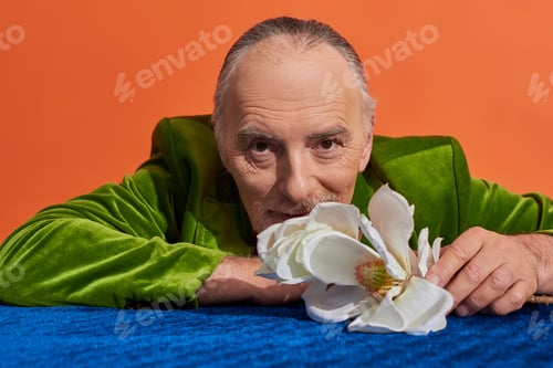 Preview: positive lifestyle, senior grey haired man in green velvet blazer smiling at camera near white