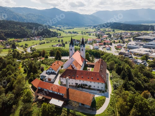 Preview: Aerial view of a picturesque village with a large church featuring twin spires, surrounded by lush g