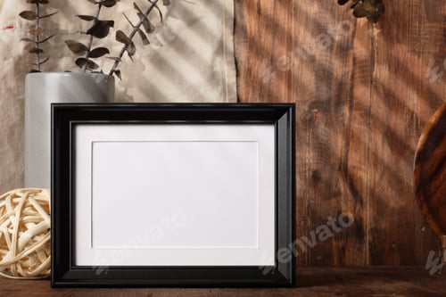 Preview: blank black photo frame with kitchenware on wood table with sunlight