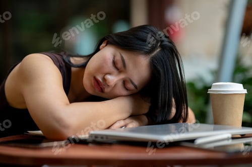 Preview: A tired Asian woman takes a nap at an outdoor table while working on her tasks.
