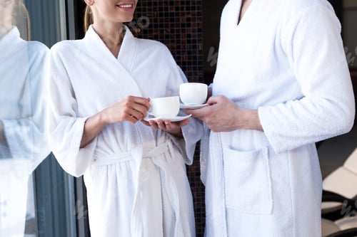 Preview: cropped shot of couple in bathrobes drinking tea in spa center