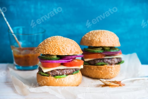 Preview: Fresh beef burger with cheese, vegetables and spicy tomato sauce on paper, blue wooden background.