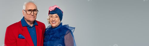 Preview: smiling elderly couple in blue dress and red blazer standing isolated on grey, banner