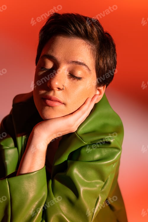 Preview: portrait of brunette woman in green leather jacket posing with closed eyes and hand near face on