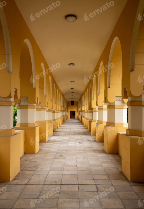 Preview: Symmetrical view of a long corridor with arches and yellow walls in a historic building