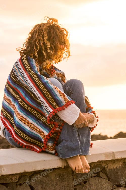 Preview: Unrecognizable lonely woman sit down on a wall looking and enjoying the sunset on the sea