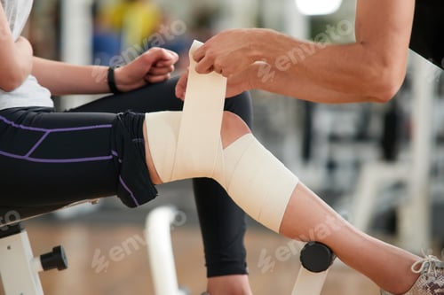 Preview: Close up man wrapping bandage on womans leg in gym.