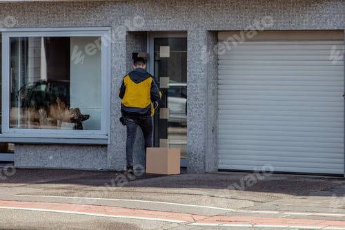 Preview: Back view of a delivery man with a box waiting in front of a closed home door