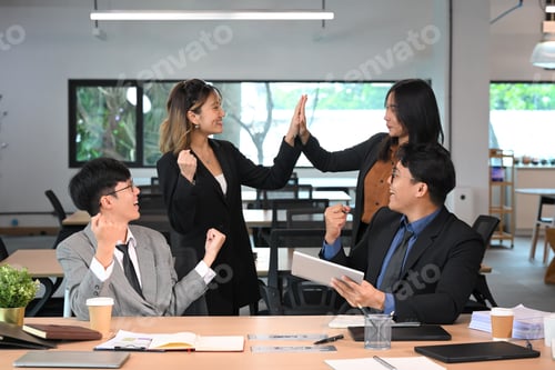 Preview: Happy coworkers cheerfully celebrating business success in a modern office