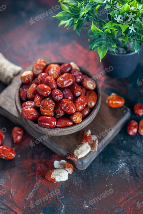 Preview: Vertical view of fresh raw silverberry fruits in a bowl on a wooden cutting board and flower pot on