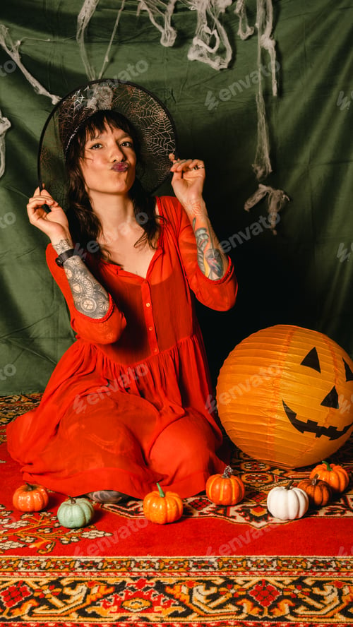 Preview: Portrait of a cute young woman in a red dress and a witch hat at a Halloween party