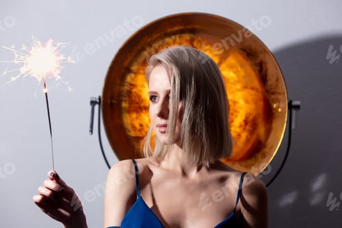 Preview: Beautiful blonde girl holds sparkler with golden sphere on background