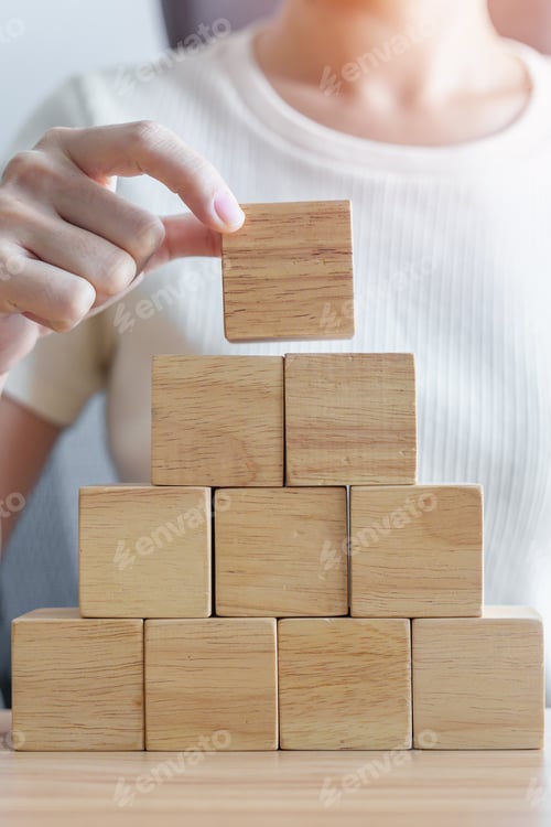 Preview: Woman hand placing wood block on the building.
