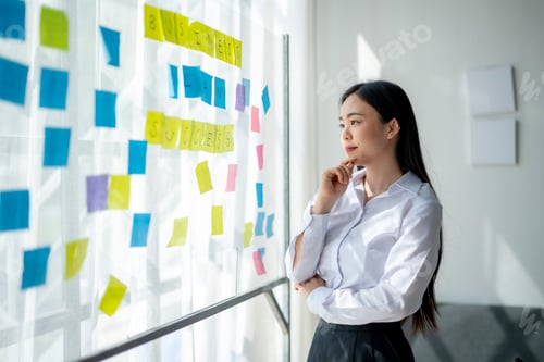 Preview: A woman is looking at a board with yellow and blue sticky notes on it