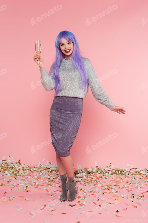 Preview: Happy stylish woman with dyed hair holding champagne near confetti on pink background