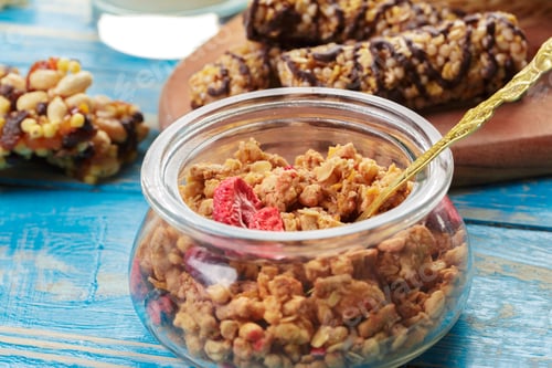 Preview: Granola in glass jar with snacks on blue wooden table during bright day