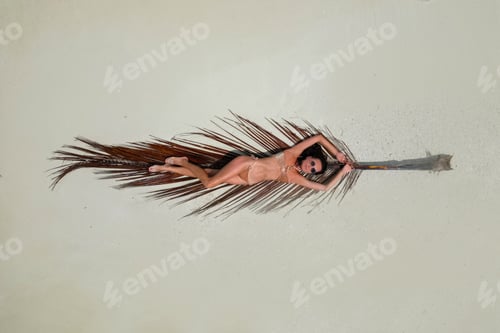 Preview: young woman tanning sunbathing on palm tree leaf woman wearing bikini at the beach on a white sand