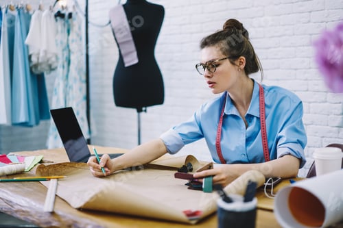 Preview: Focused dressmaker working at table in modern studio