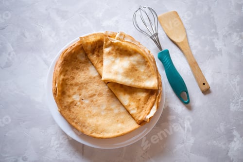 Preview: Round thin pancakes lie on a plate. Nearby lies a whisk and a spatula for cooking.