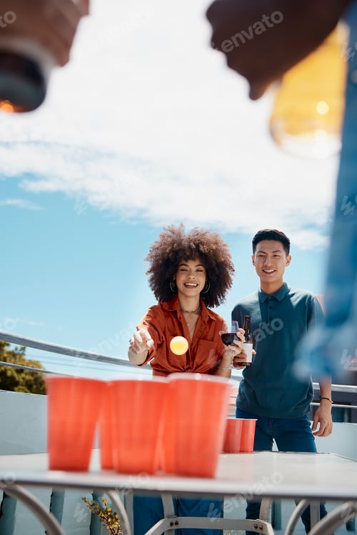 Preview: Happy young friends playing beer pong together outside. Diverse friends throwing a ball into cups o