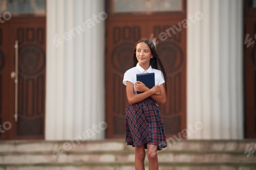 Visualização: Concepção de conhecimento. Menina da escola em uniforme está ao ar livre perto do prédio