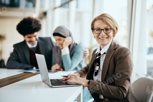 Preview: Happy senior insurance agent using laptop while having meeting with clients and looking at camera.