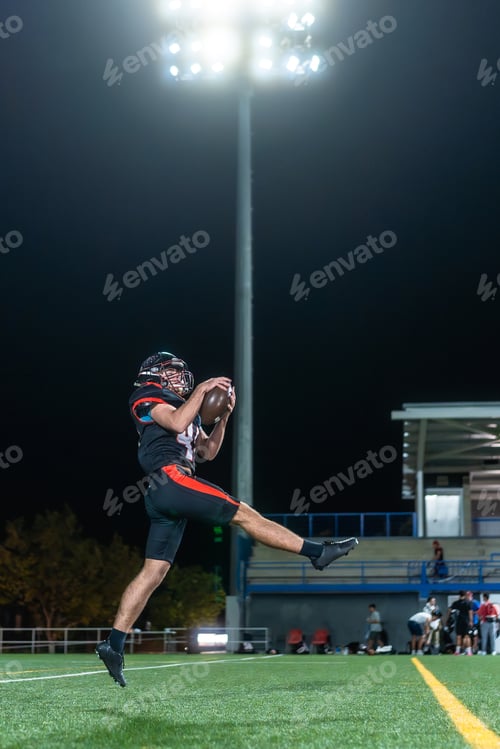 Preview: American football player catching ball during night game