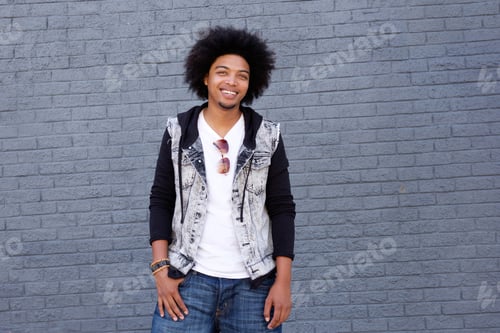 Preview: Young man with afro smiling standing in front of gray wall