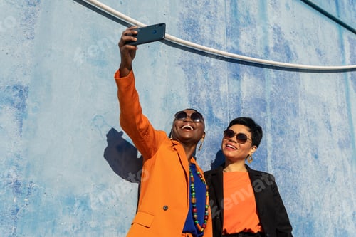 Preview: Low angle of cheerful stylish multiracial adult girlfriends with short hair in sunglasses and