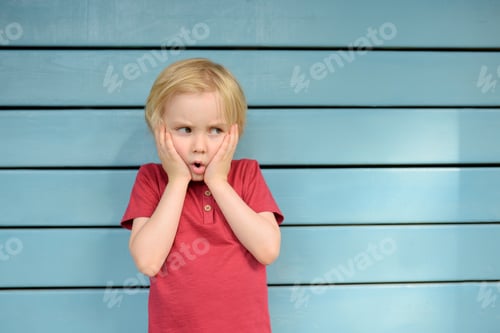Preview: Angry and upset little boy wearing red t-shirt standing on blue background. Facepalm gesture