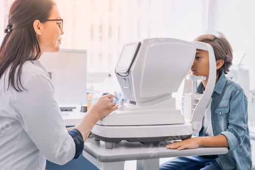 Preview: Side view shot of little boy having test for eyes with special optical apparatus by female doctor