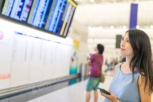 Preview: Woman checking flight schedule with cellphone and display board