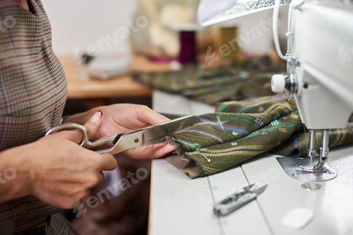 Preview: Seamstress working on modern electrical sewing machine making exclusive garments in fashion studio.