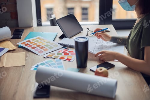 Preview: Close up shot of interior designer wearing protective mask working with color samples and blueprint
