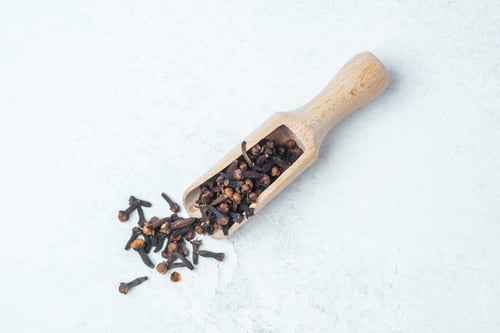 Preview: Cloves spilling from a wooden scoop on a light surface in a kitchen setting