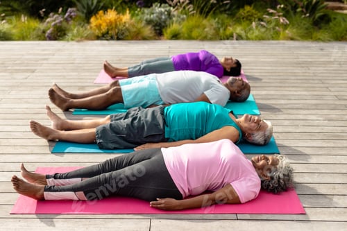 Preview: Multiracial senior friends with eyes closed exercising while lying on mats on hardwood floor in yard
