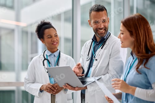 Preview: Happy doctor using laptop with female colleagues while working at the clinic.