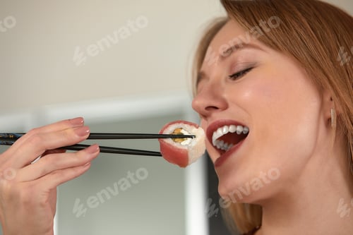 Preview: Attractive woman resting at home with sushi. Eating sushi with chopsticks close up, food takeout and