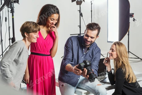Preview: Photographer, stylists and model reviewing photo shoot on digital SLR in photography studio